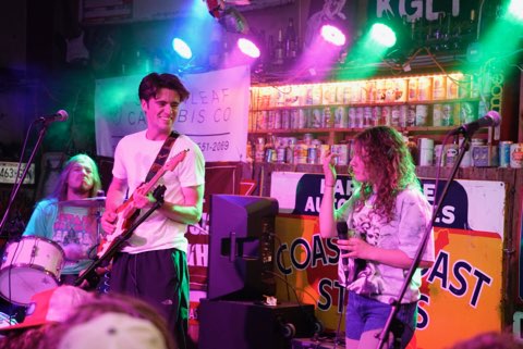 Jack Ooster playing electric guitar with a band under colorful stage lights