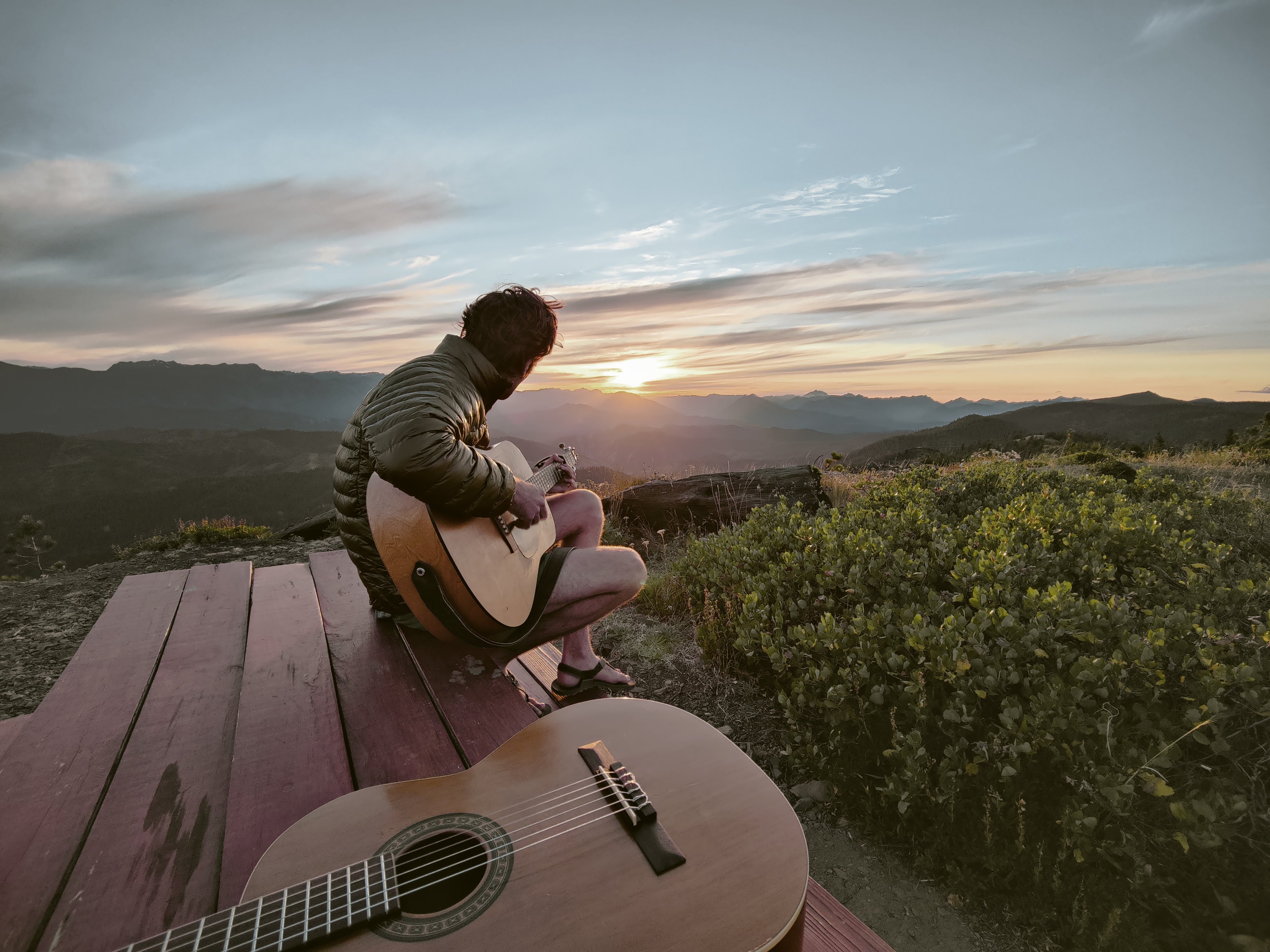 Jack Ooster sitting with an acoustic guitar at a mountain overlook